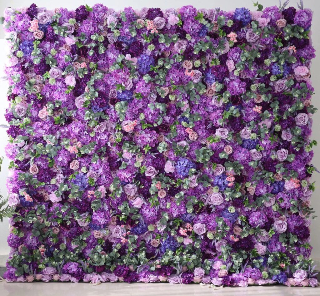 A floral wall with an array of purple and pink flowers interspersed with green leaves, forming a dense, colorful backdrop.